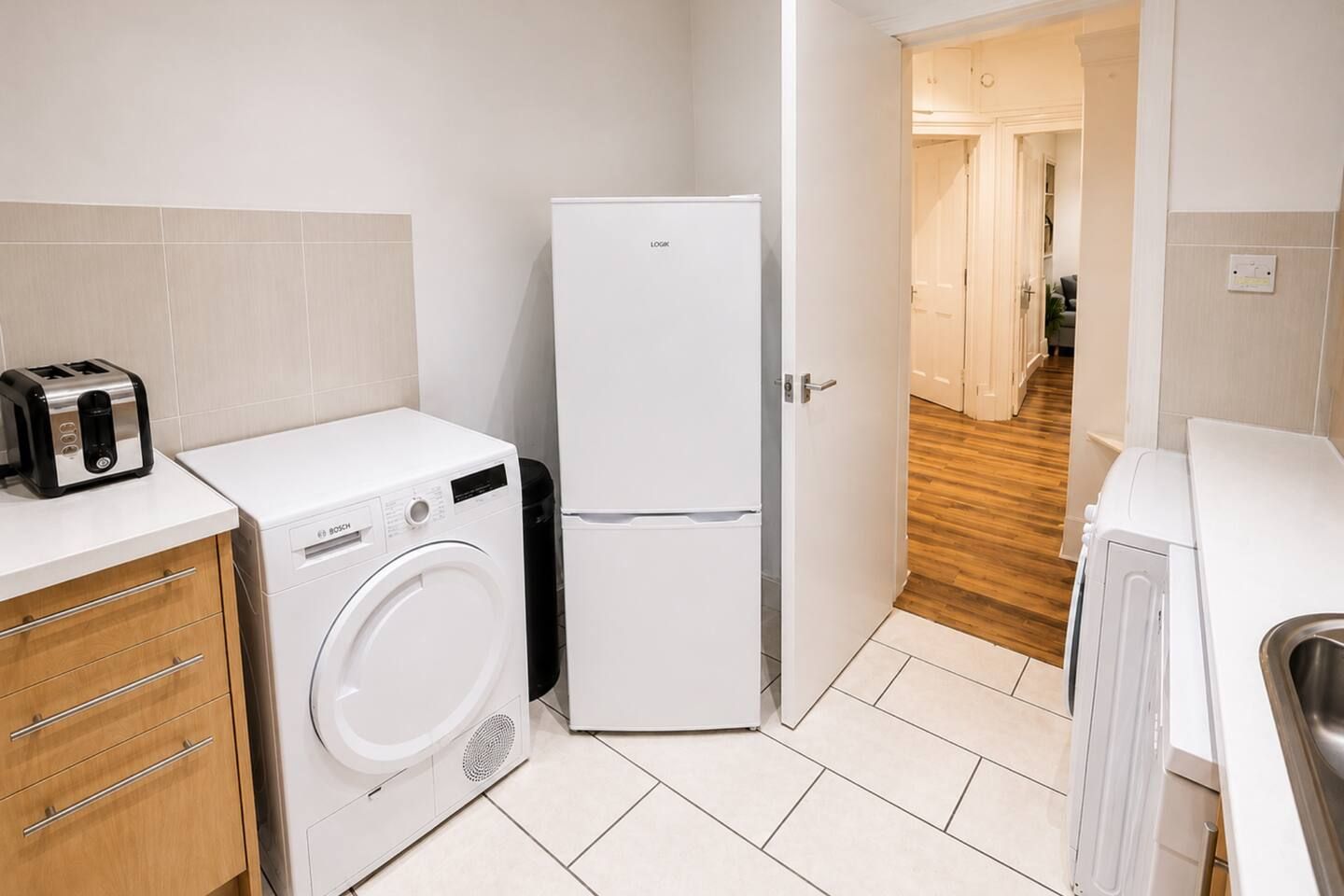 A compact kitchen with a Bosch washing machine, a white refrigerator, and a toaster.