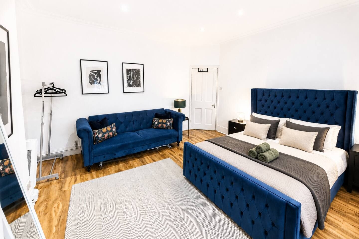 A bedroom with a bed, a sofa, a bedside table, a lamp, and two framed pictures on the wall.