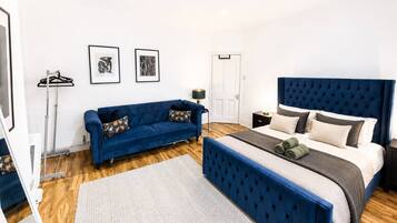 A bedroom with a bed, a sofa, a bedside table, a lamp, and two framed pictures on the wall.