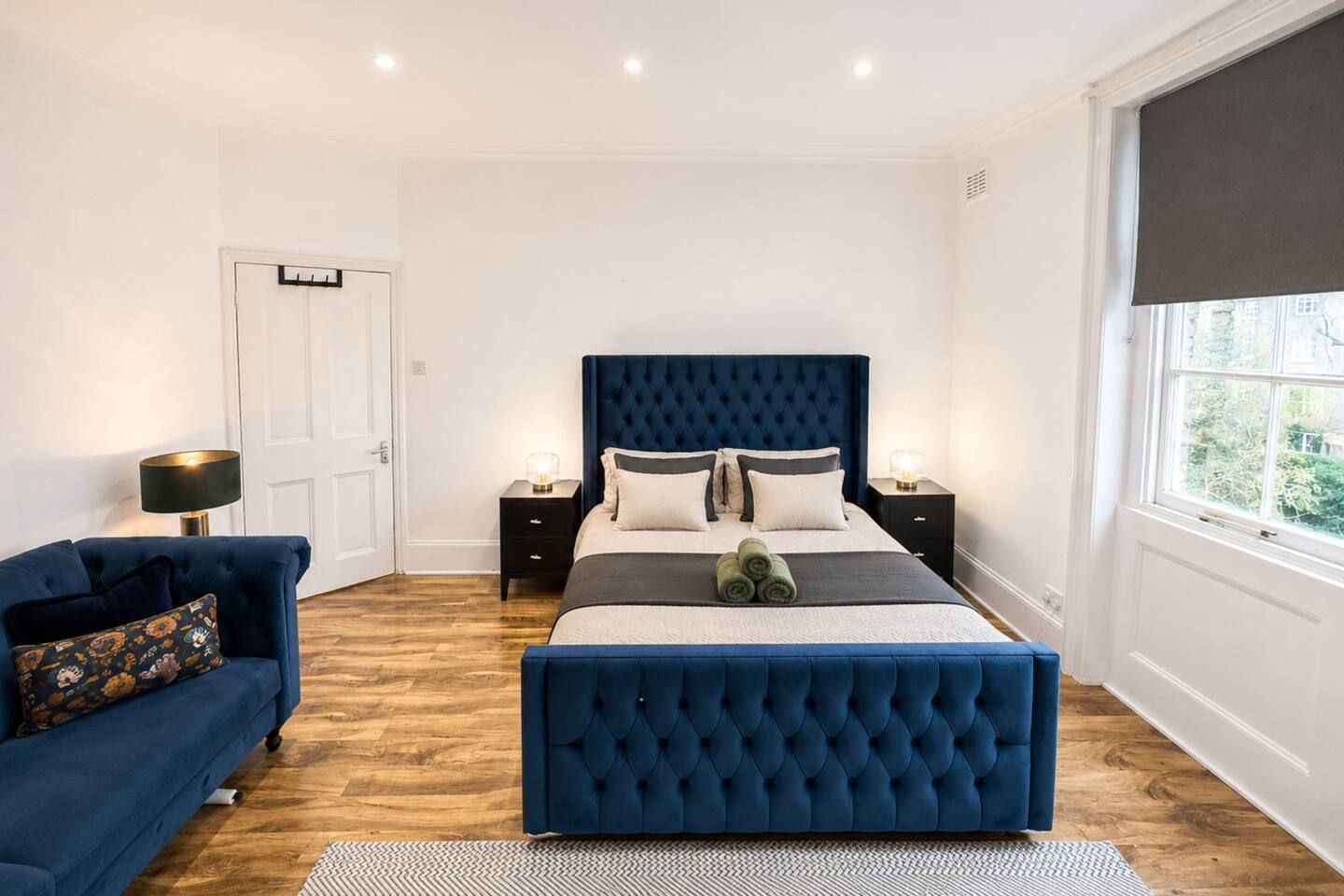 A bedroom with a large bed, a blue sofa, two bedside tables, and a window with a view.