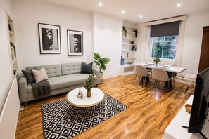 Un salon moderne avec un canapé gris, une table basse ronde et un coin repas comprenant une table et des chaises blanches.