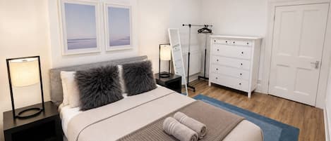 A bedroom with a bed, nightstands, a dresser, a mirror, and a door.