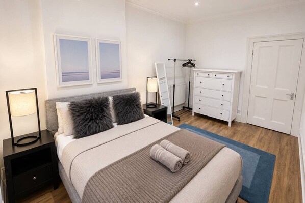 Une chambre à coucher avec un lit, des tables de chevet, une commode, un miroir et une porte.