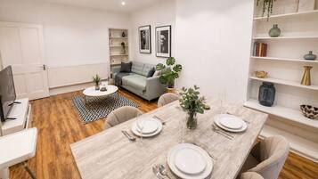 A modern living room with a dining area, a grey sofa, a coffee table, and a bookshelf.