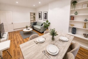 A modern living room with a dining area, a grey sofa, a coffee table, and a bookshelf. - 2-bed Maida Vale Flat | little venice, paddington (London)