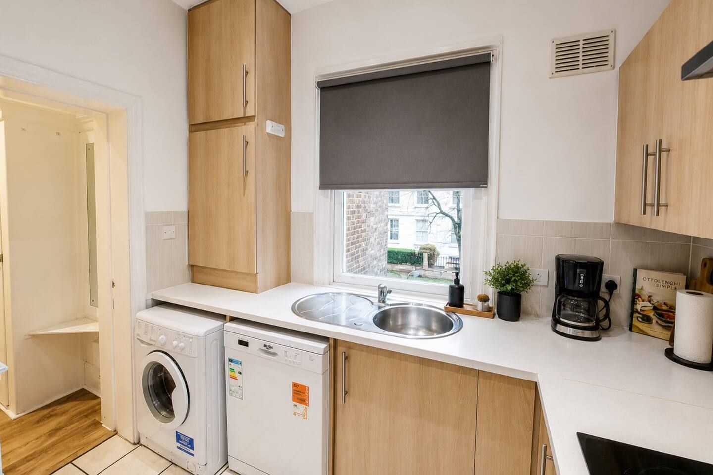 A compact kitchen with a washing machine, a sink, and a coffee maker.