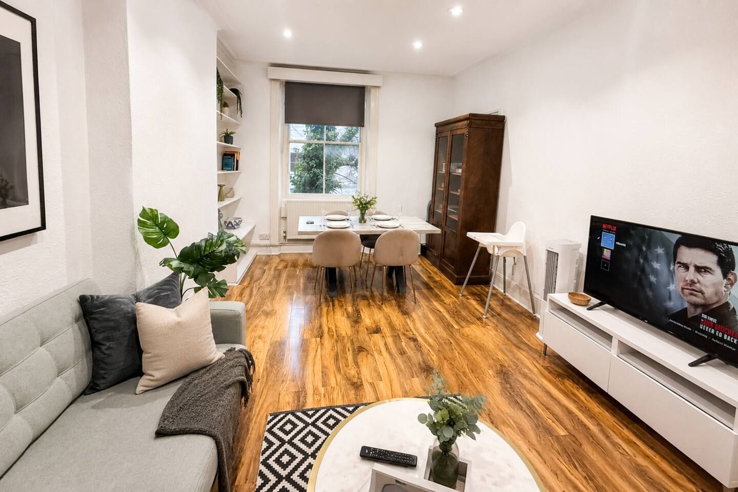 A modern living room with a sofa, coffee table, TV, dining area, and a bookshelf.