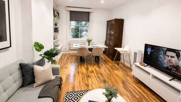 A modern living room with a sofa, coffee table, TV, dining area, and a bookshelf.
