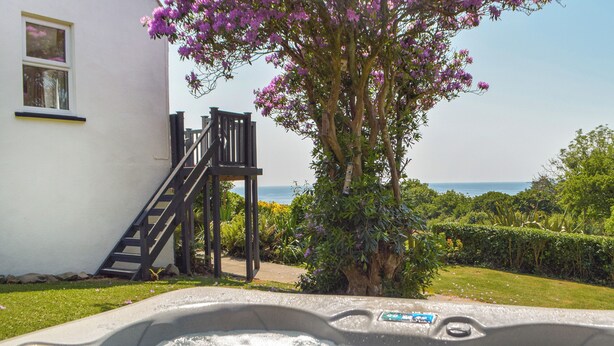 Un jacuzzi con vista al mar, un edificio blanco con una escalera y un árbol con flores moradas.