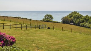 Un campo cubierto de hierba con una cerca de madera, una construcción pequeña y vista al mar.