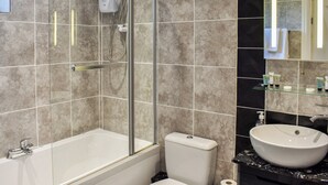 A modern bathroom with a bathtub, toilet, and a glass shelf with toiletries. - Roxy's Cottage - UK44687 (Beamish)
