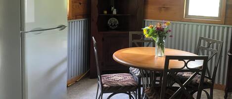 Una cocina compacta con refrigerador, armarios de madera, un reloj, una mesa de madera con sillas y una ventana con vista.