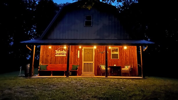 Une grange en bois avec un porche, un banc et une table entourée de chaises.
