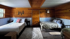 Une cabane avec deux lits, un plafond en bois, une fenêtre et une porte.