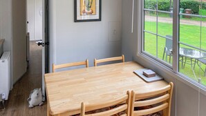 Zona pranzo con tavolo e sedie in legno, un quadro appeso alla parete e vista giardino attraverso una finestra.