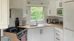 Una cucina con mobili bianchi, un fornello, un lavello e una finestra vista verde.