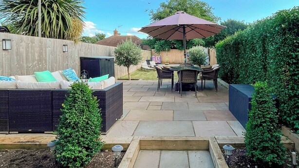 Un espace patio aménagé avec un canapé, des chaises et une table, le tout placé sous un grand parasol.