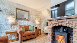 Un salon chaleureux avec un mur en pierre, une cheminée, un canapé en cuir et un téléviseur à écran plat.