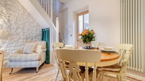 Un coin repas avec une table ronde, des chaises et un vase de fleurs. On y trouve un escalier avec une rampe et une vue sur l’extérieur.