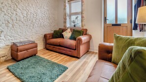 Un salon chaleureux avec un mur en pierre, un canapé en cuir marron, un tapis vert et une porte en bois.
