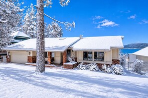Una casa de dos pisos con techo nevado, cimientos de ladrillo y un garaje.