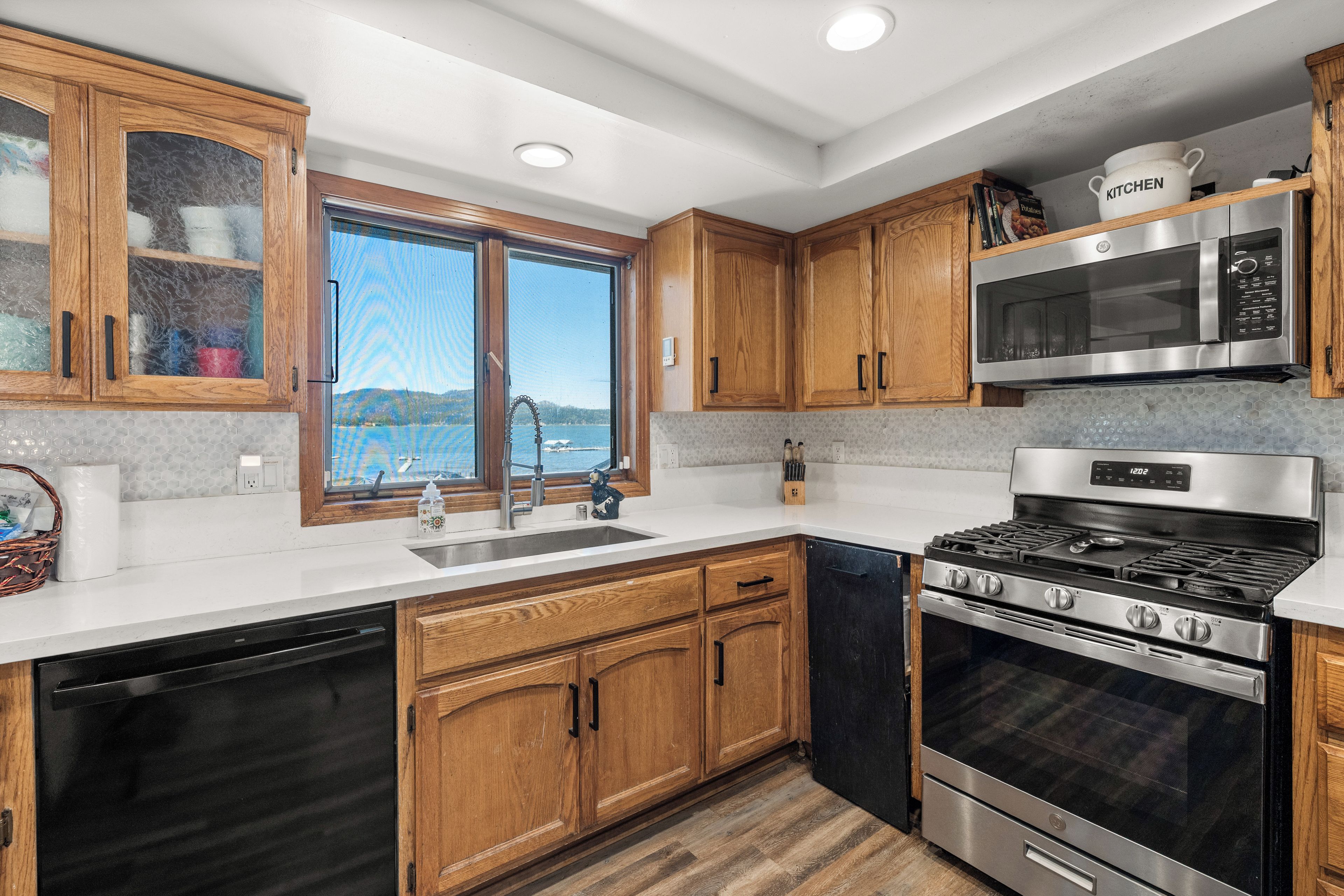 A modern kitchen with wooden cabinets, a stainless steel stove, a microwave, and a large window overlooking a lake.