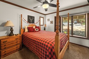 A bedroom with a four-poster bed, wooden nightstands, a dresser, and a view of the outside through large windows.