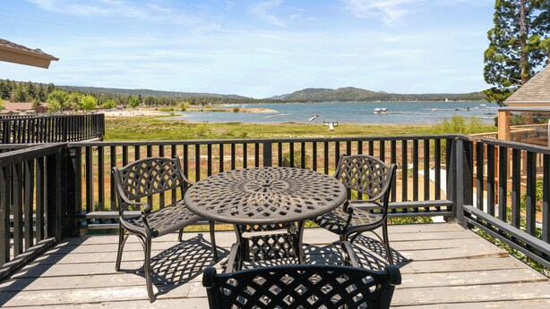 A deck with a round table and chairs, overlooking a body of water with boats and a distant shoreline.