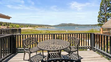 A deck with a round table and chairs, overlooking a body of water with boats and a distant shoreline.