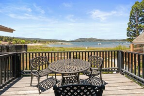 A deck with a round table and chairs, overlooking a body of water with boats and a distant shoreline.