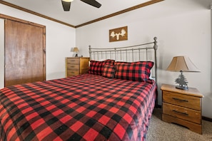A bedroom with a bed, a nightstand, a dresser, a ceiling fan, and a wall-mounted lamp.
