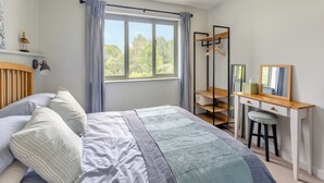 Una camera da letto con un letto, una scrivania, una sedia, una lampada a sospensione, una finestra con tende e uno scaffale decorato con un uccellino.