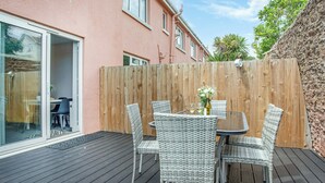 A patio with a table and chairs, a wooden fence, and a house in the background. - Garden Apartment - UK44654 (Paignton)