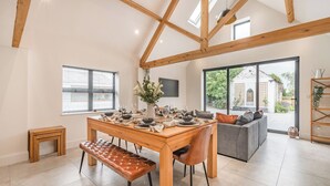 Un grand espace à manger avec une table en bois dressée pour quatre personnes, un banc et un canapé gris en arrière-plan.