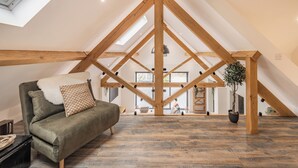 Un loft spacieux avec un plafond haut, des poutres apparentes, un canapé vert et une plante en pot.