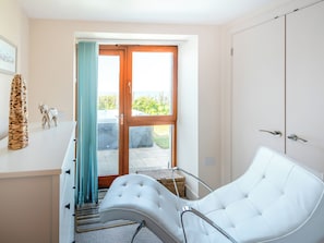 A room with a white chair, a wooden door, a window with curtains, and a small statue on the wall.