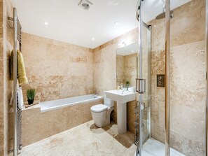 Moderni kylpyhuone, jossa on lasiseinällä varustettu suihku, erillinen kylpyamme, wc ja peilillä varustettu pesuallas.