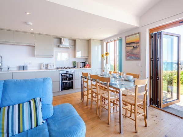 A modern kitchen with a dining area, a sofa, and a view of the outdoors.