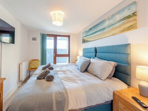 Een slaapkamer met een bed, een schilderij, een televisie, een lamp en een raam.