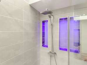Eine moderne Dusche mit Handbrause und Duschkabine mit violetter Beleuchtung.