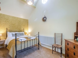 A bedroom with a bed, a radiator, a wooden chair, a dresser, and a wall with a wreath.