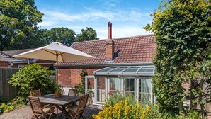 A patio with a table and chairs, a conservatory, and a brick house. - The Old Reading Room (Salhouse, near Norwich)