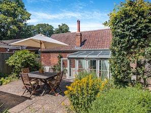 A patio with a table and chairs, a conservatory, and a brick house.
