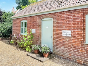 A brick building with a green door, two windows, and potted plants. There are signs on the wall commemorating Queen Victoria's 60th anniversary.