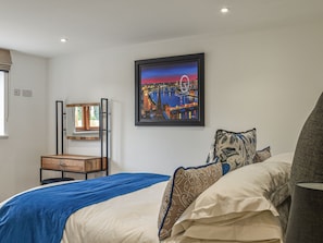 A bedroom with a bed, pillows, a bedside table, a mirror, and a framed picture on the wall.