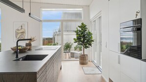 Moderni keittiö, jossa on suuri keittiösaareke, sisäänrakennettu uuni ja näkymä ulos.