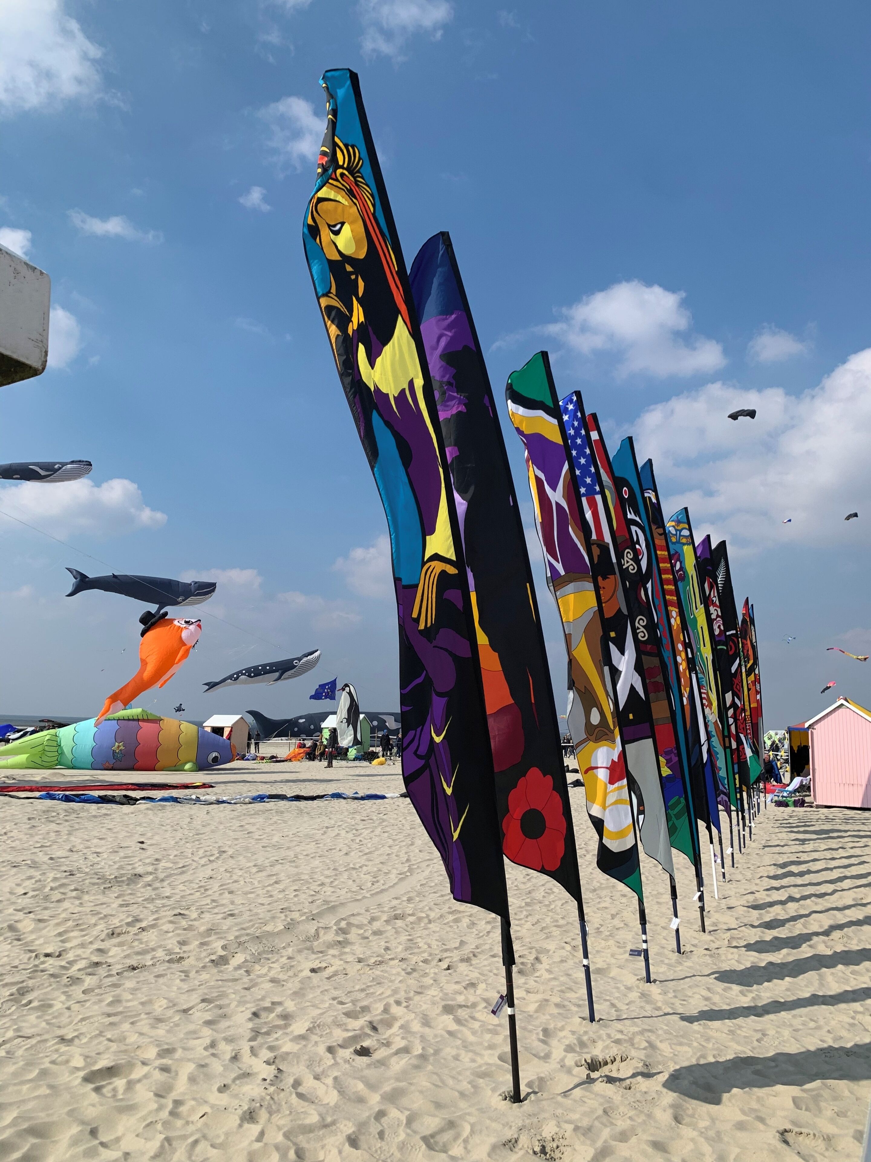 Una playa con banderas coloridas y una cometa con forma de ballena.