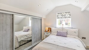 A bedroom with a bed, a nightstand, a mirror, and a window with a view of the outside. - Discover Yorkshire’s charms from this cosy holiday let. (Warmfield, near Wakefield)