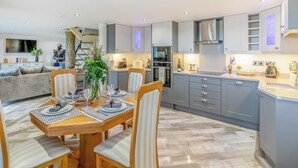 A modern kitchen with grey cabinets, a built-in oven, and a dining area with a wooden table and chairs. - Discover Yorkshire’s charms from this cosy holiday let. (Warmfield, near Wakefield)