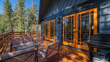 Una terraza de madera con mobiliario exterior, ventanas amplias y una parrilla.